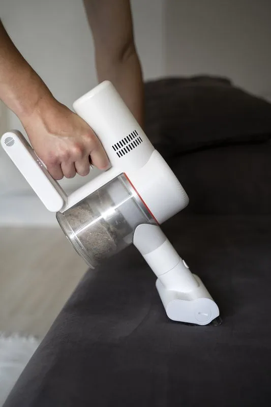 Person using a white handheld vacuum to clean a dark gray sofa.