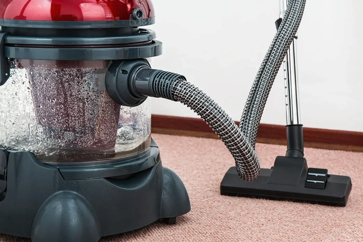 A red and black wet/dry vacuum cleaner with hose and nozzle on a pink carpet.